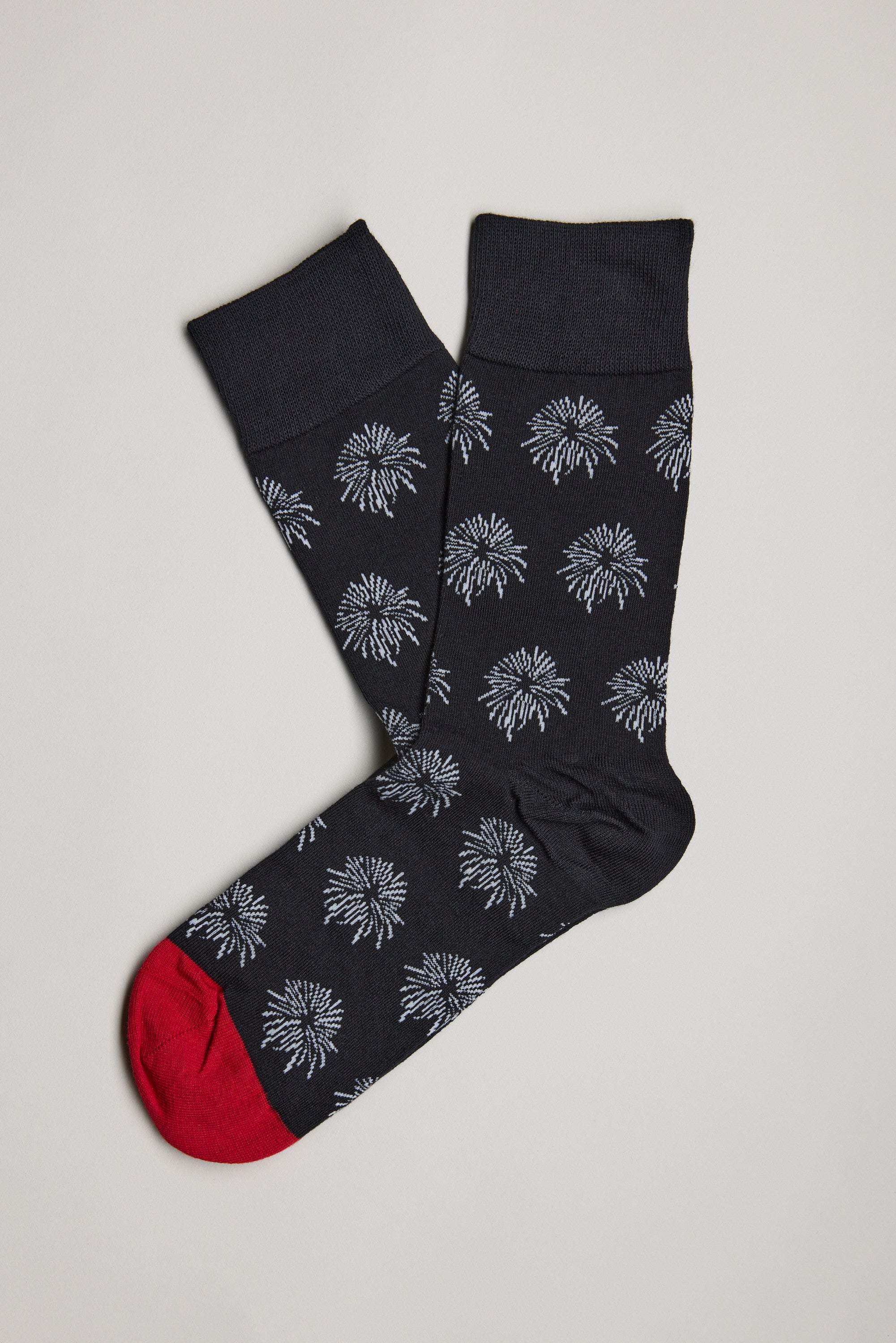 A pair of Barkers Hudson Firework Socks—black cotton socks with a white firework burst pattern and bright red toes—are laid flat on a neutral background.