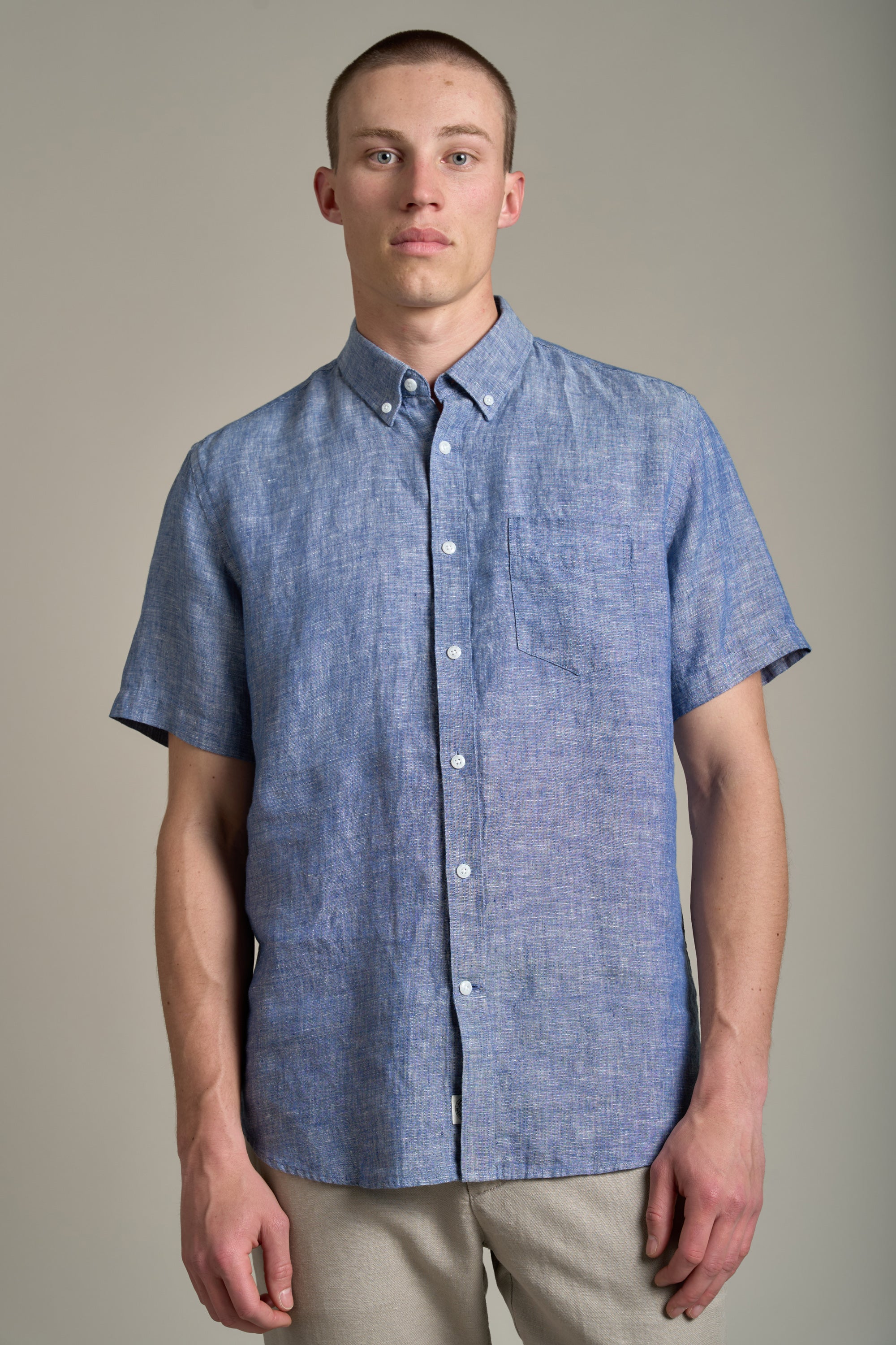 A man wears the Barkers Gentry Linen Shirt, a light blue, breathable, lightweight shirt with a chest pocket, and stands against a plain gray background looking at the camera.