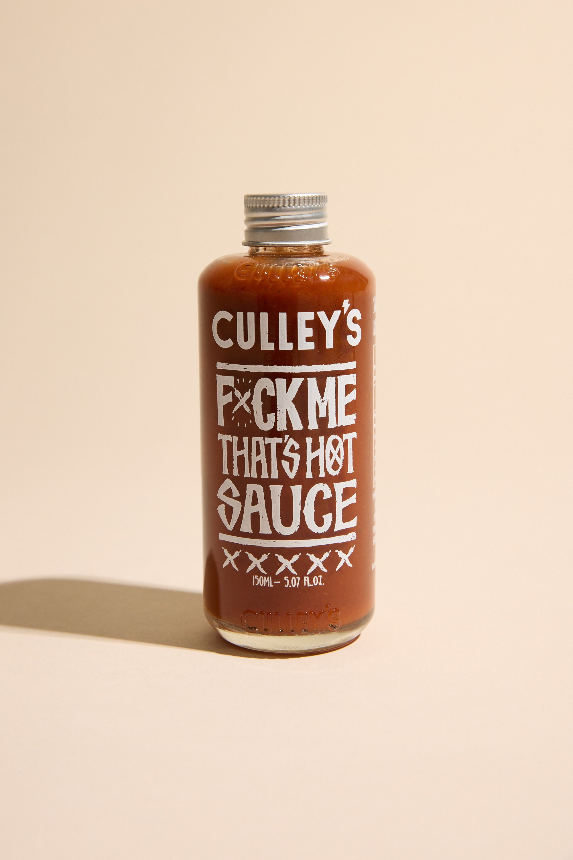 A bottle of Culley's F@#k Me That's Hot Sauce features bold white text on a light beige label. This New Zealand hot sauce packs Carolina Reaper heat in fiery red sauce, sealed with a metal cap.