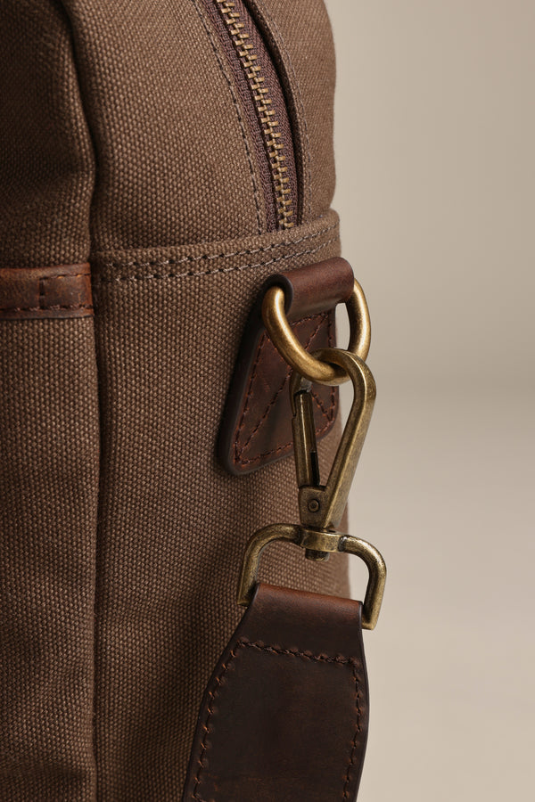 Close-up of the Barkers Redford Canvas Laptop Bag in brown, featuring a premium leather strap attachment, detailed stitching, brass clasp, and metal hardware set against a neutral background.