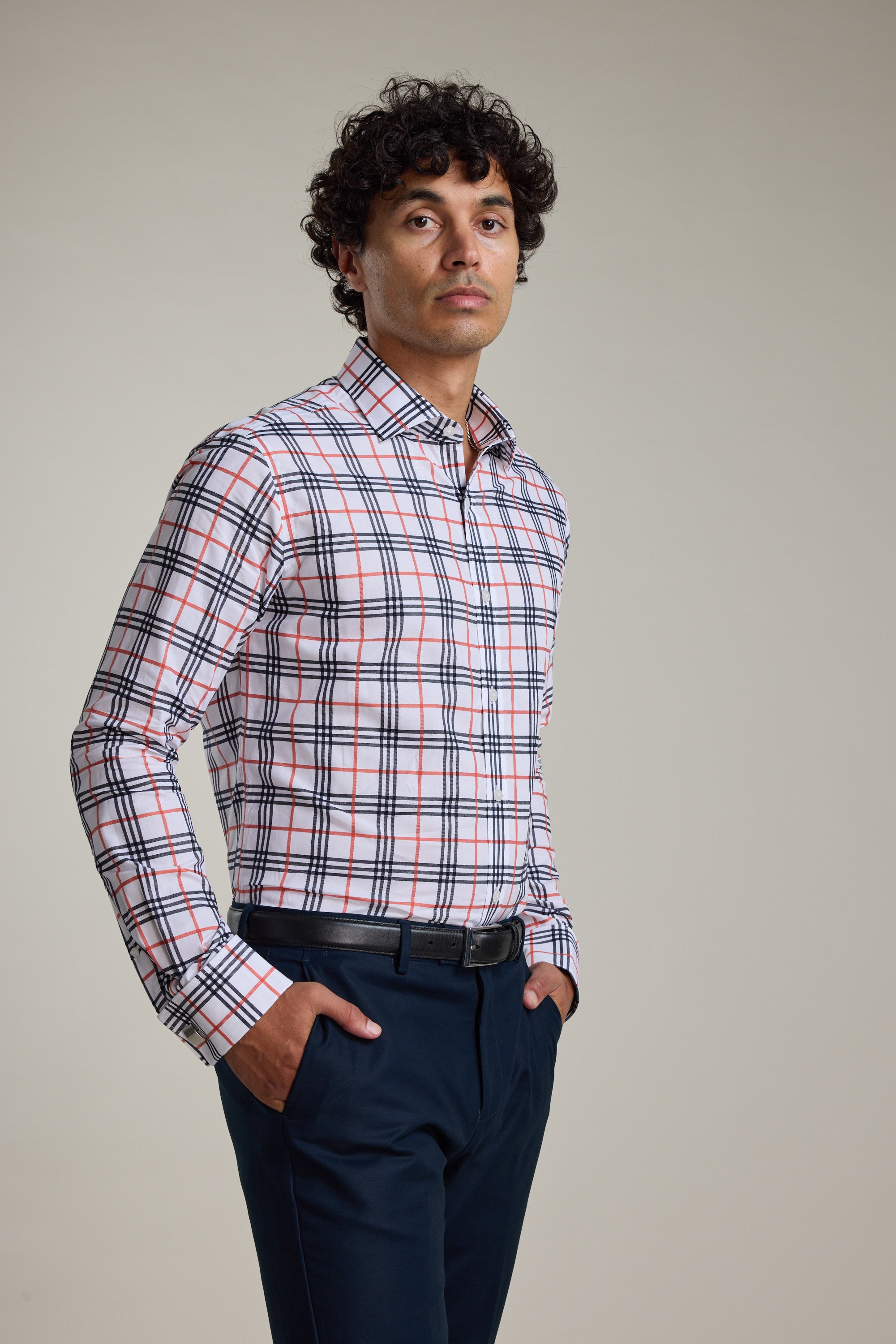 A man stands with hands in pockets, wearing the Barkers Wilma French Cuff Business Shirt—white, tailored fit with red, blue, and black plaid—and dark pants, set against a plain light background.