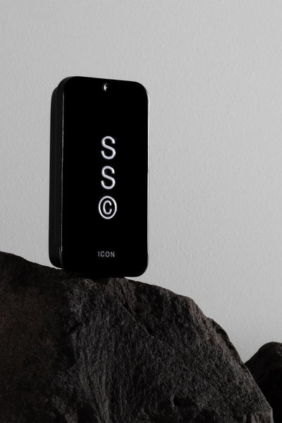 A sleek black rectangular Solid State - Icon cologne device labeled “ICON” stands upright on a dark rock, with illuminated “S S ©” letters, set against a plain light gray background.