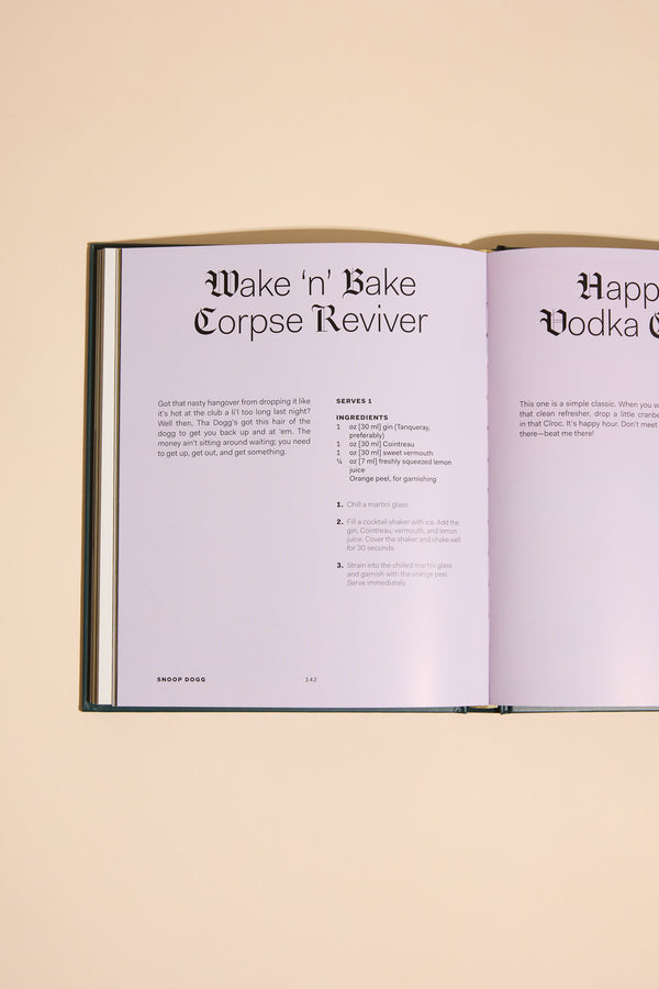 An open copy of From Crook to Cook by Other rests on a beige surface, displaying the Wake n Bake Corpse Reviver recipe with ingredients and instructions on a light purple background.