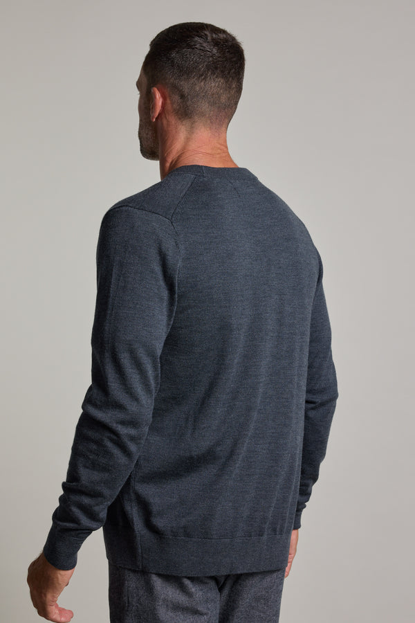 A man with short dark hair, seen from behind, wears the Barkers Skyland ZQrx Merino Cardi in dark gray and gray pants against a plain light background.