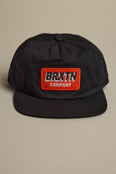 The Brixton Payment MP Snapback, a black 5-panel hat with a flat brim, features a red and white BRXTN COMPANY patch on the front. It is shown against a neutral beige background.