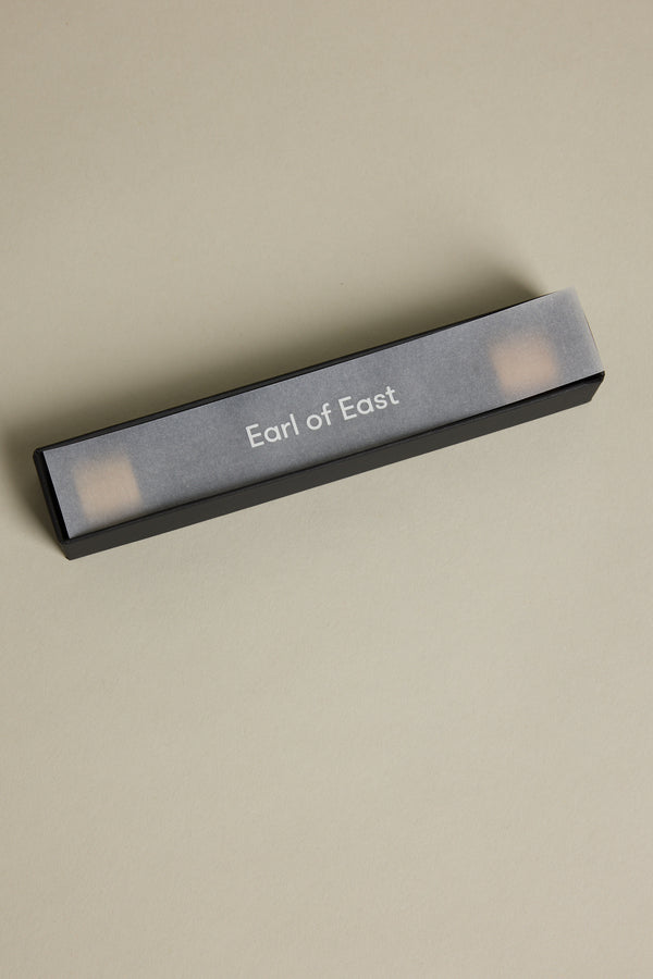 A black rectangular box with a translucent gray cover labeled Earl of East rests on a light beige surface, offering EoE Onsen Japanese Incense Sticks for a refreshing peppermint scent experience.