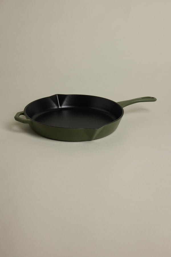 The IronClad Satin Enamel Cast Iron - 28cm Legacy Pan satin, featuring a green finish, handle and helper handle, sits on a beige surface. Its black interior is induction-ready and ideal for non-stick cooking.