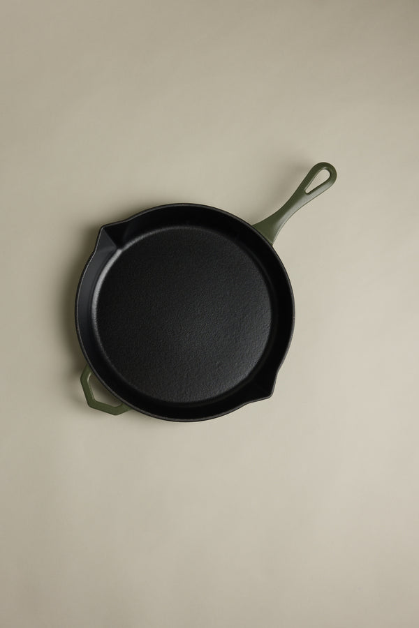 The IronClad Satin Enamel Cast Iron - 28cm Legacy Pan satin, featuring a black body and green handles, is shown from above on a light beige background.