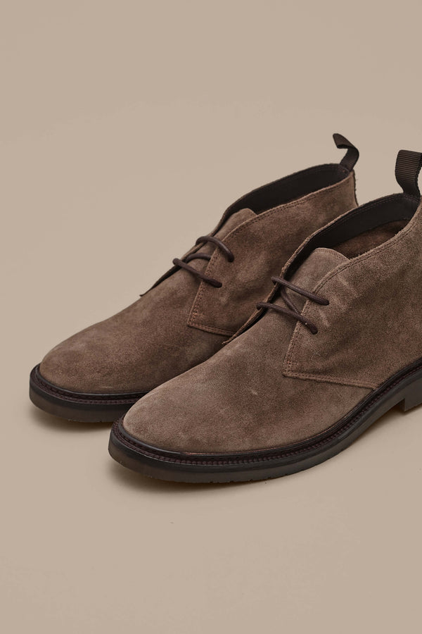 The Barkers Howarth Desert Boot, a quality brown suede pair with dark brown soles and pull tabs, is displayed on a beige background.