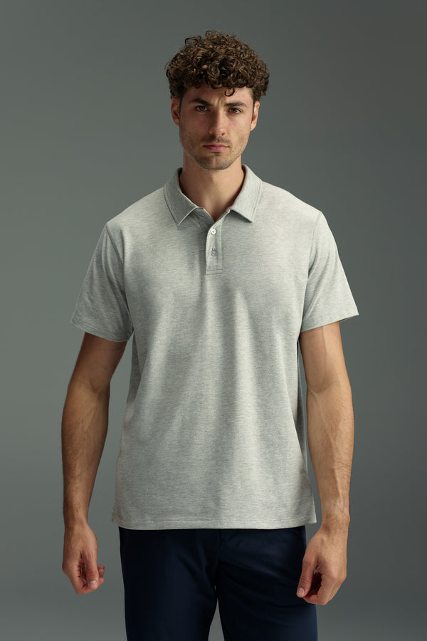 A man with curly brown hair wears the WearEver Outbound Polo by WearEver—a light gray, breathable, quick-drying, stretch fabric shirt—and dark pants, standing against a plain gray background, facing the camera with a neutral expression.