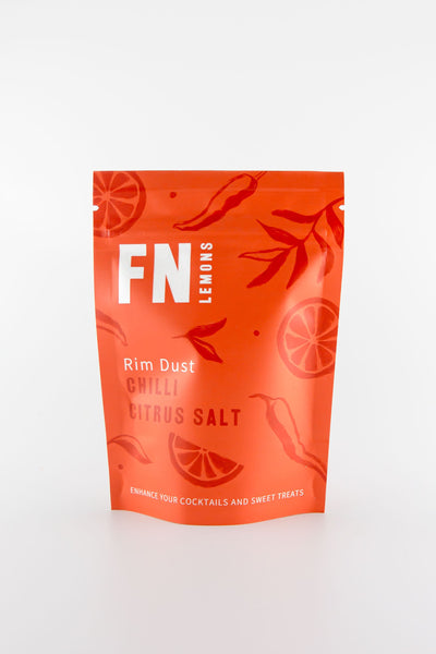 A vibrant orange F N Lemons - Chilli Citrus Salt pouch stands upright against a white backdrop, adorned with chili peppers and citrus slices—ideal for spicing up cocktail rims or using as a flavorful garnish.