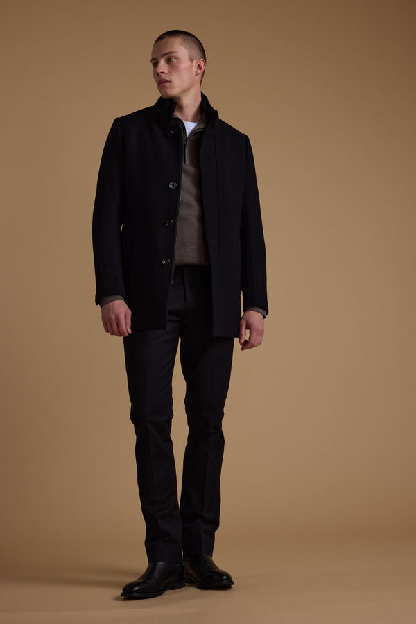 A man wearing the Barkers Raymond Coat stands against a plain brown background, paired with a brown sweater, white shirt, black pants, and black shoes. He looks to his left with a neutral expression.