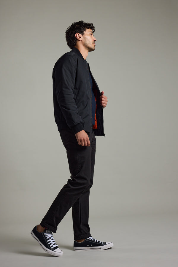 Man in a Barkers Dunhill Bomber Jacket, black pants, and sneakers stands sideways, plain background.