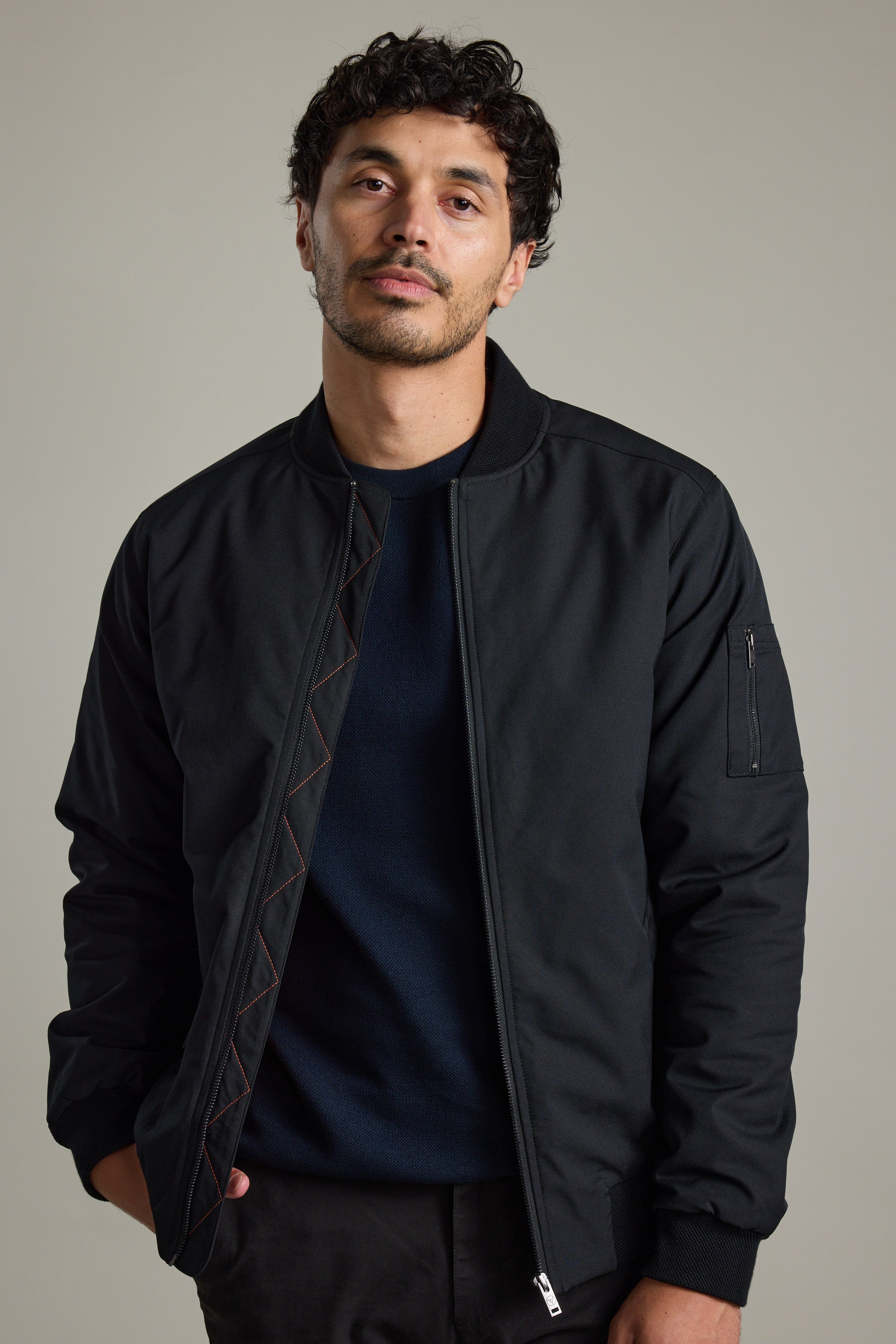 Man with short curly hair wears a Barkers Dunhill Bomber Jacket and navy shirt against a plain background.