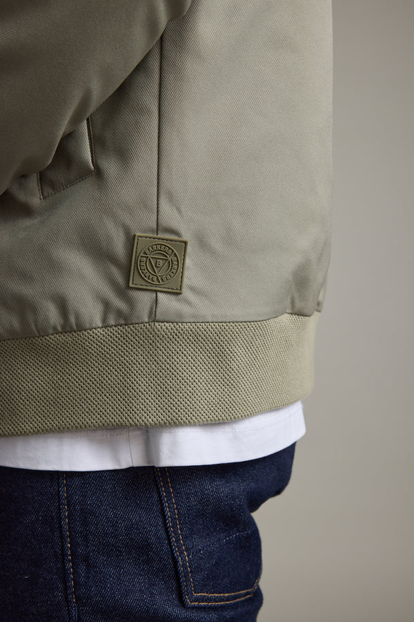 Close-up of a person in a Barkers Dunhill Bomber Jacket, white shirt, and dark blue jeans.