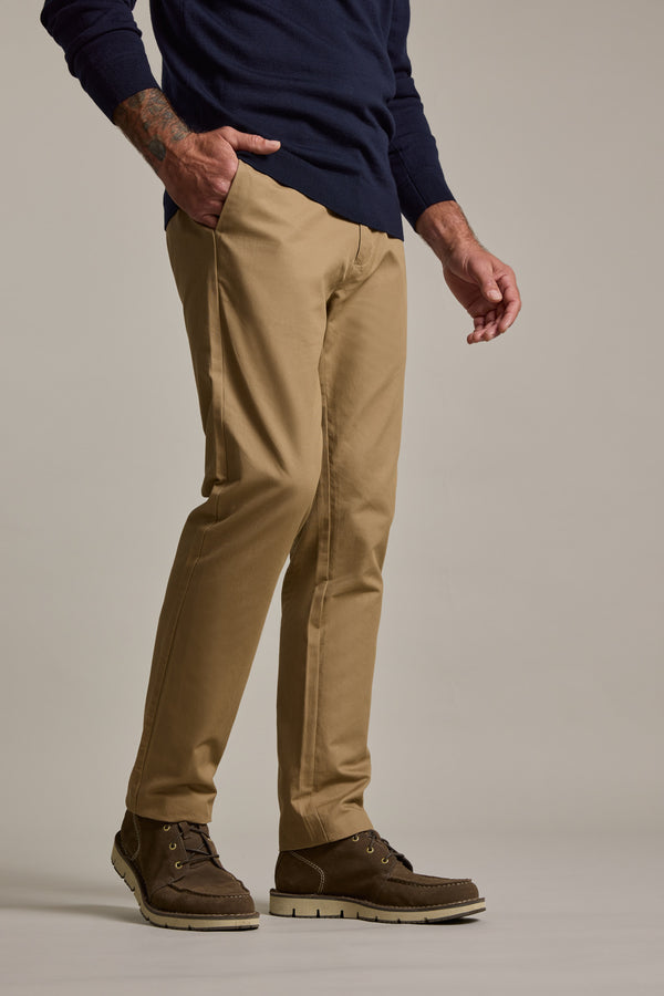 A person wearing a navy sweater, Barkers Dundas Chino in tan khaki, and dark brown lace-up boots stands with one hand in their pocket against a plain background.