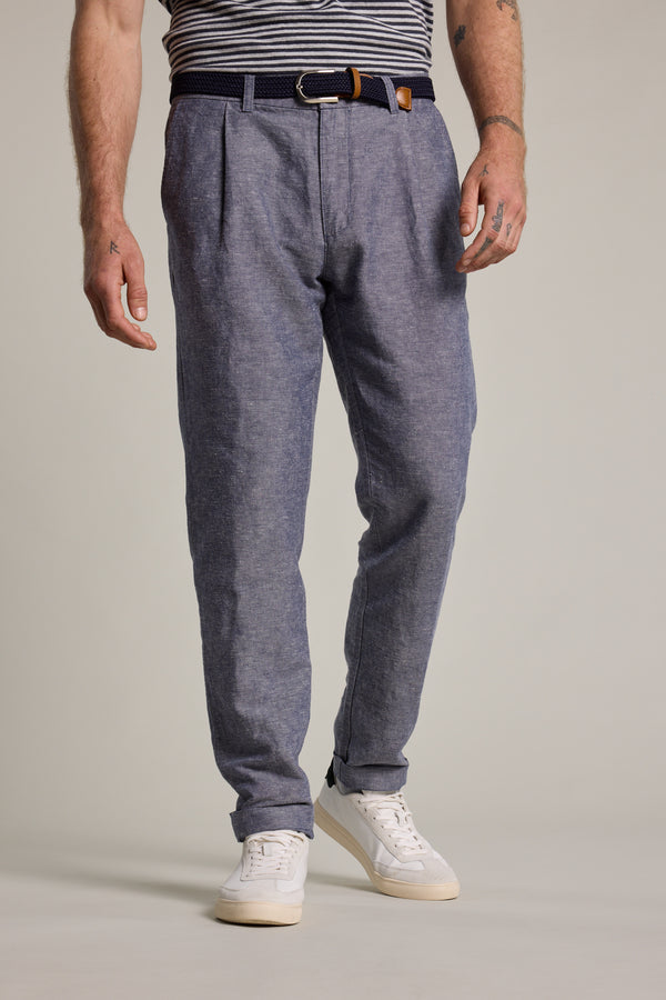 A person stands against a plain light background, wearing Barkers' Newman Linen Pants in blue, paired with a navy belt, striped shirt, and white sneakers. The image is cropped from the shoulders down.