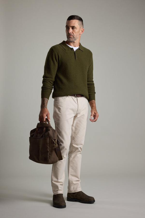 Man in Barkers Ainsley Woollen Long Sleeve Polo, holding a brown bag on a gray background.
