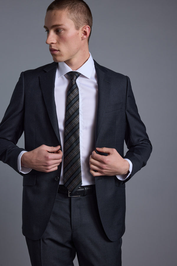 A man wearing the Barkers Mayfair ZQ Suit Jacket stands against a plain gray background, looking to his left as he adjusts his jacket with both hands.
