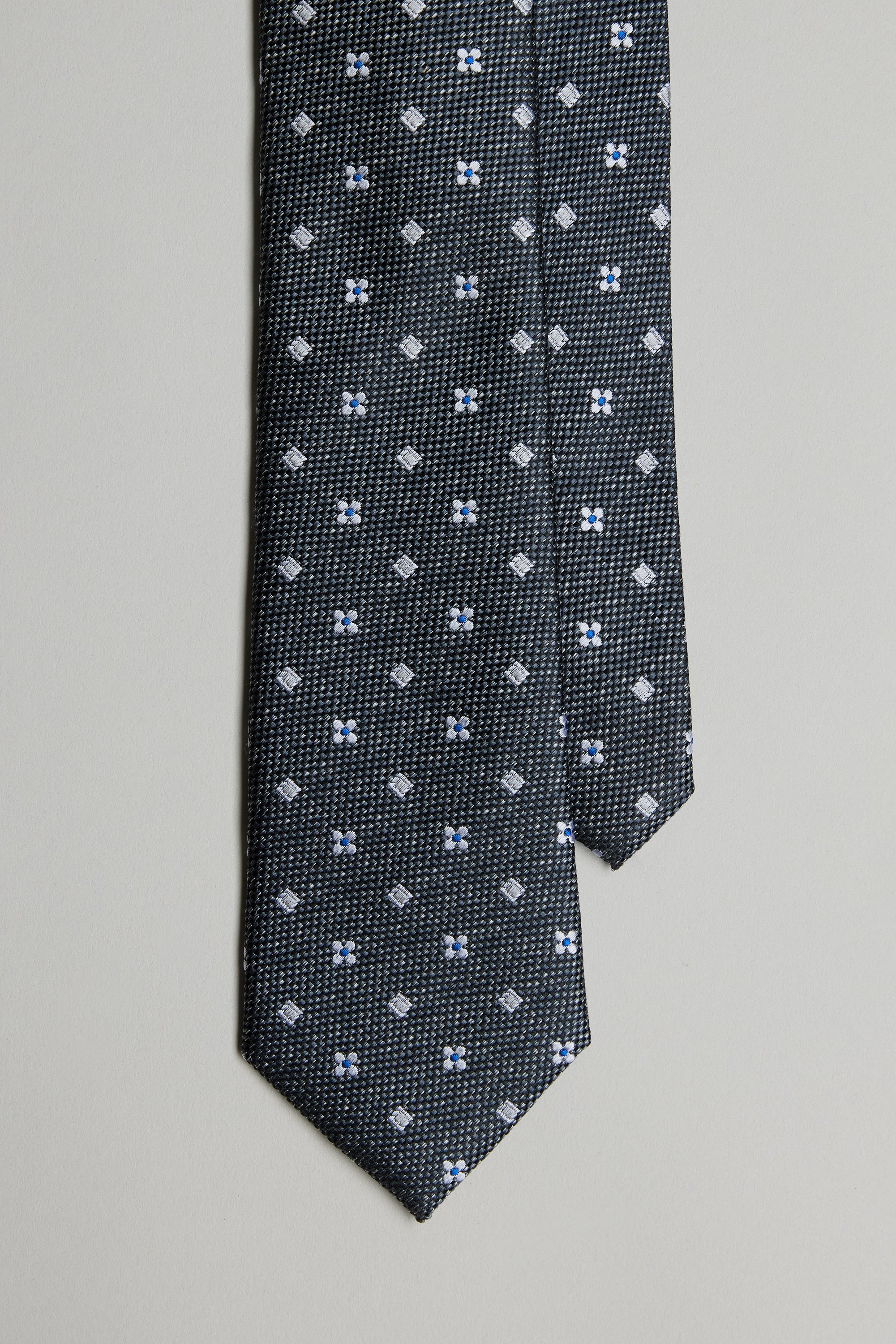 The Barkers Enright Flower Tie features a dark base with a small white and blue geometric floral pattern, shown against a plain light background.