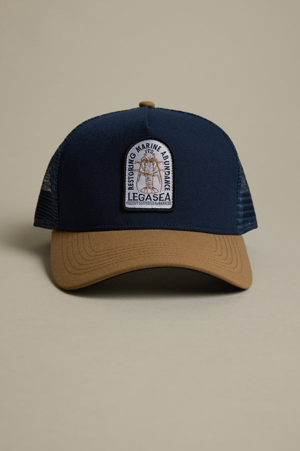 The Legasea Crayfish Trucker Snapback Cap by Legasea is a navy blue and tan adjustable mesh-back hat with an F.F.S. patch reading “Restoring Marine Abundance, LegaSea,” featuring a fish graphic, shown on a neutral background.