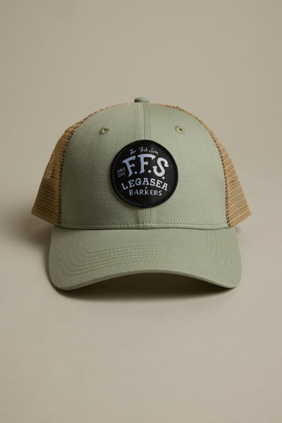 The Legasea FFS Trucker Cap by Legasea features khaki green and tan mesh with a round black patch reading “F.F.S LEGASEA BARKERS” in white, shown against a plain beige background.