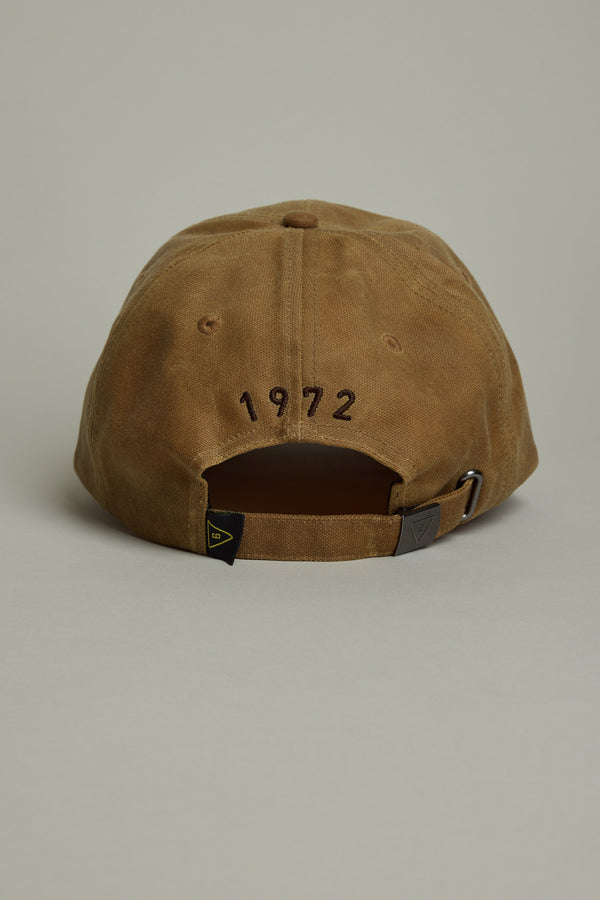 The Barkers Benson Waxed Cotton Cap is a brown heritage-style baseball cap with "1972" embroidered above the back opening, an adjustable strap, and a small tag at the bottom.