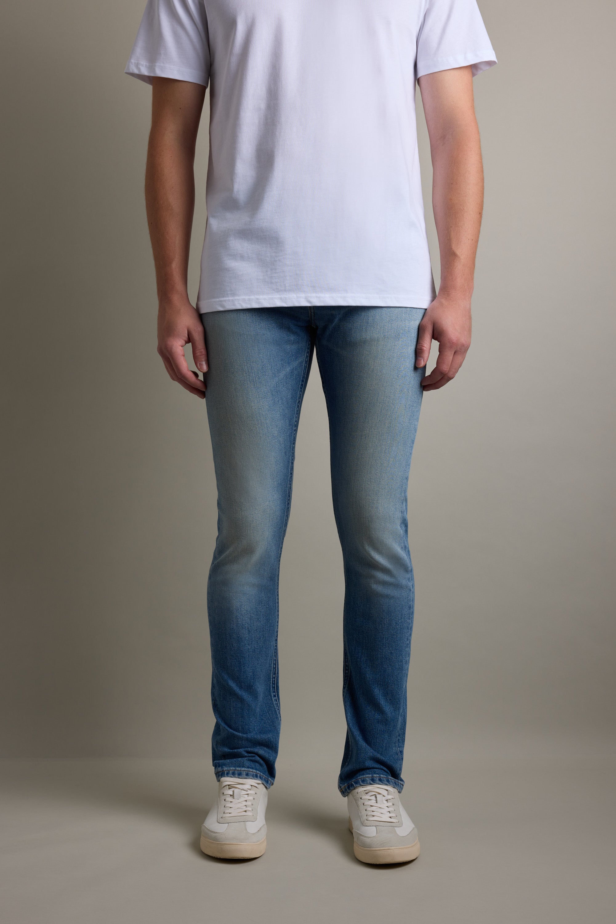 Person in a white t-shirt, Barkers Rambler Denim Slim Jean, and white sneakers on plain background.
