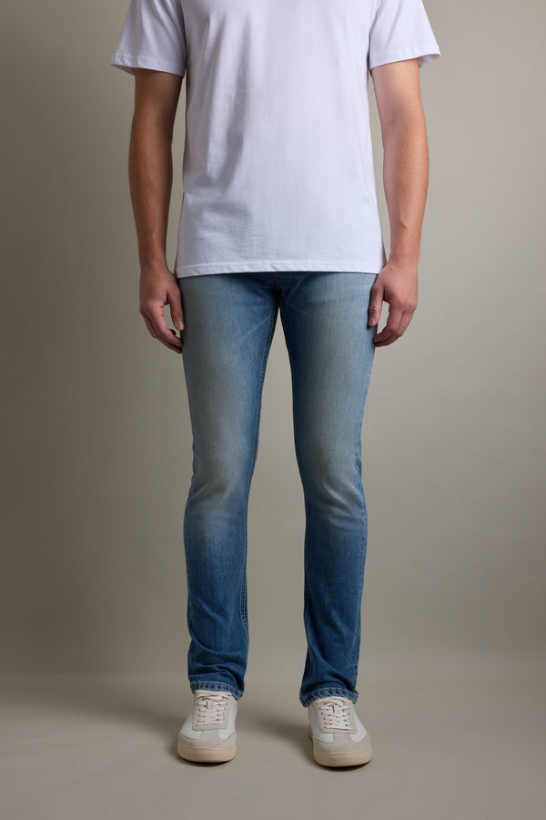 Person in a white t-shirt, Barkers Rambler Denim Slim Jean, and white sneakers on plain background.