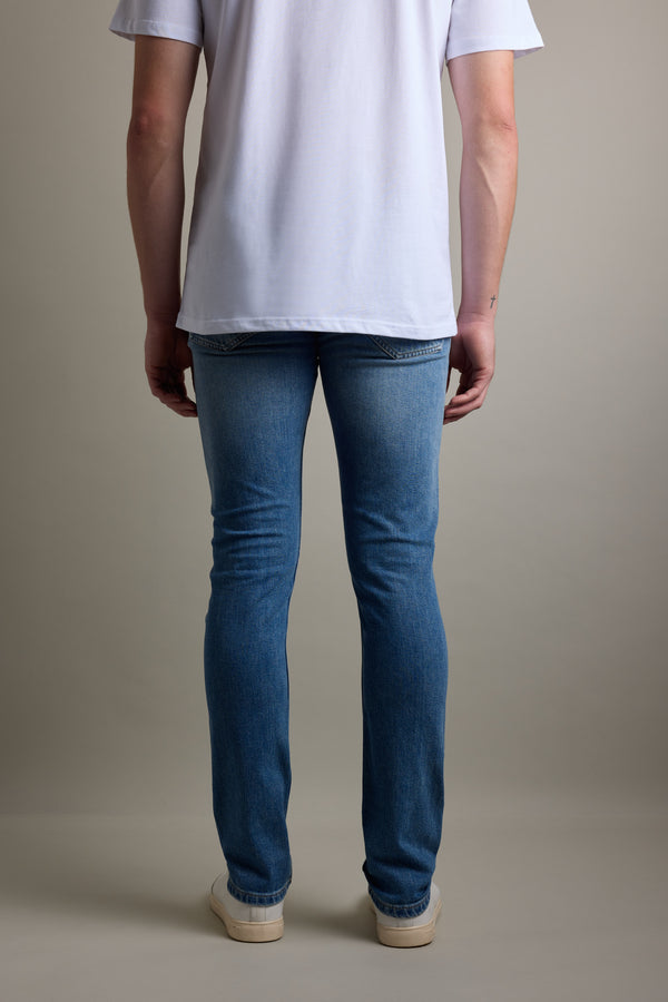 Person in a white t-shirt, Barkers Rambler Denim Slim Jean, and sneakers, seen from the back.