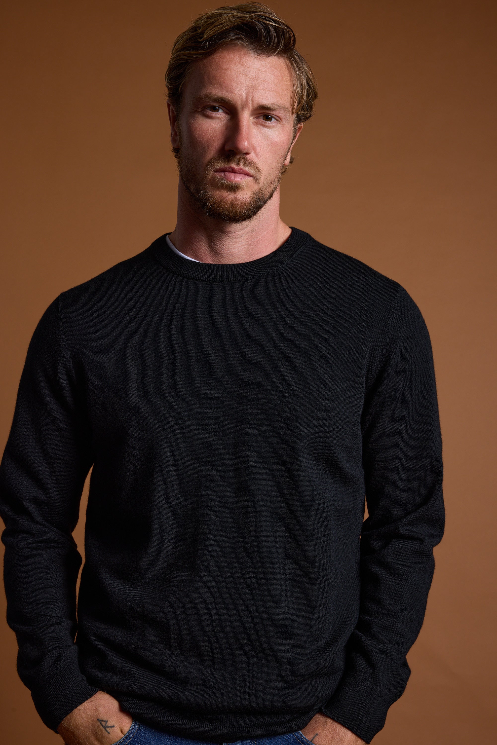 Man with short hair and beard wears a Barkers Skyland ZQrx Merino Crew against a brown background.