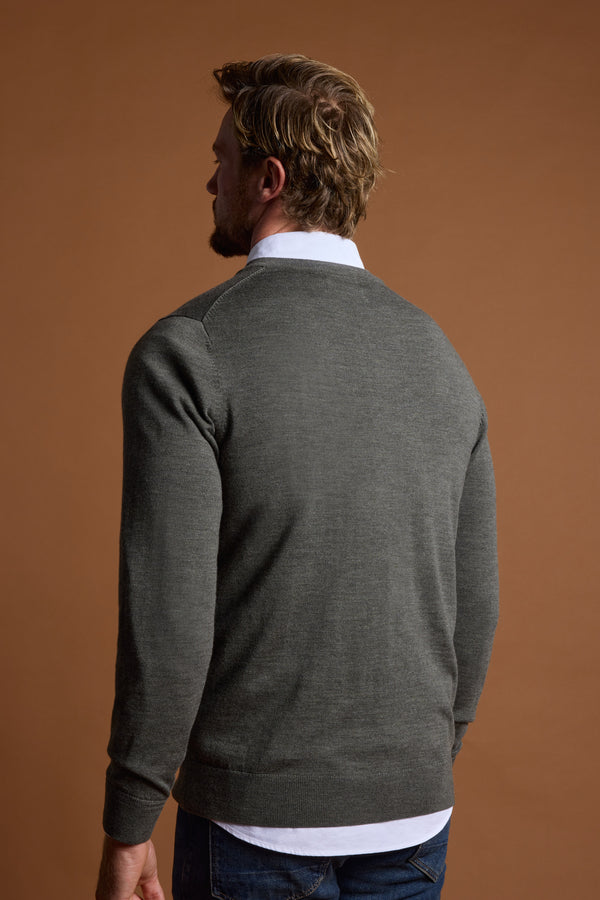 A man with light brown hair and a short beard stands with his back to the camera, wearing the Barkers Skyland ZQrx Merino Vee sweater in gray over a white collared shirt, set against a plain brown background.