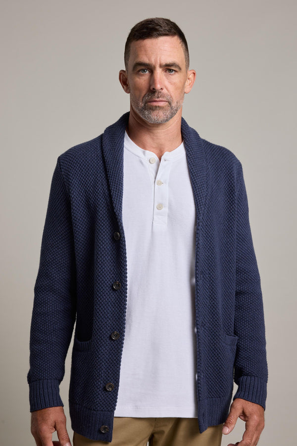 A man with short dark hair and a trimmed beard models Barkers’ Brighton Cotton Shawl Cardi in navy over a white henley and tan pants, set against a plain light gray background—perfect for winter layering.