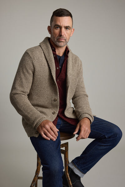 Man in Barkers Rudder Cotton Shawl Cardi and jeans sits on a stool, ready for winter layering.