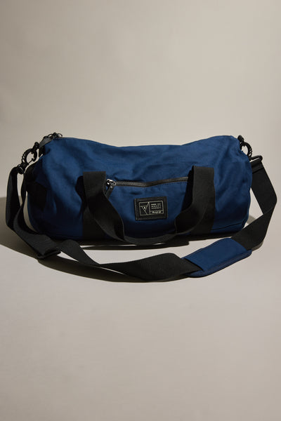 The Barkers Canvas Duffle Bag is a blue cotton travel bag with black handles, a shoulder strap, a front zip pocket, and a fabric label. Durable and stylish, it's perfect for any trip. Displayed on a neutral background.