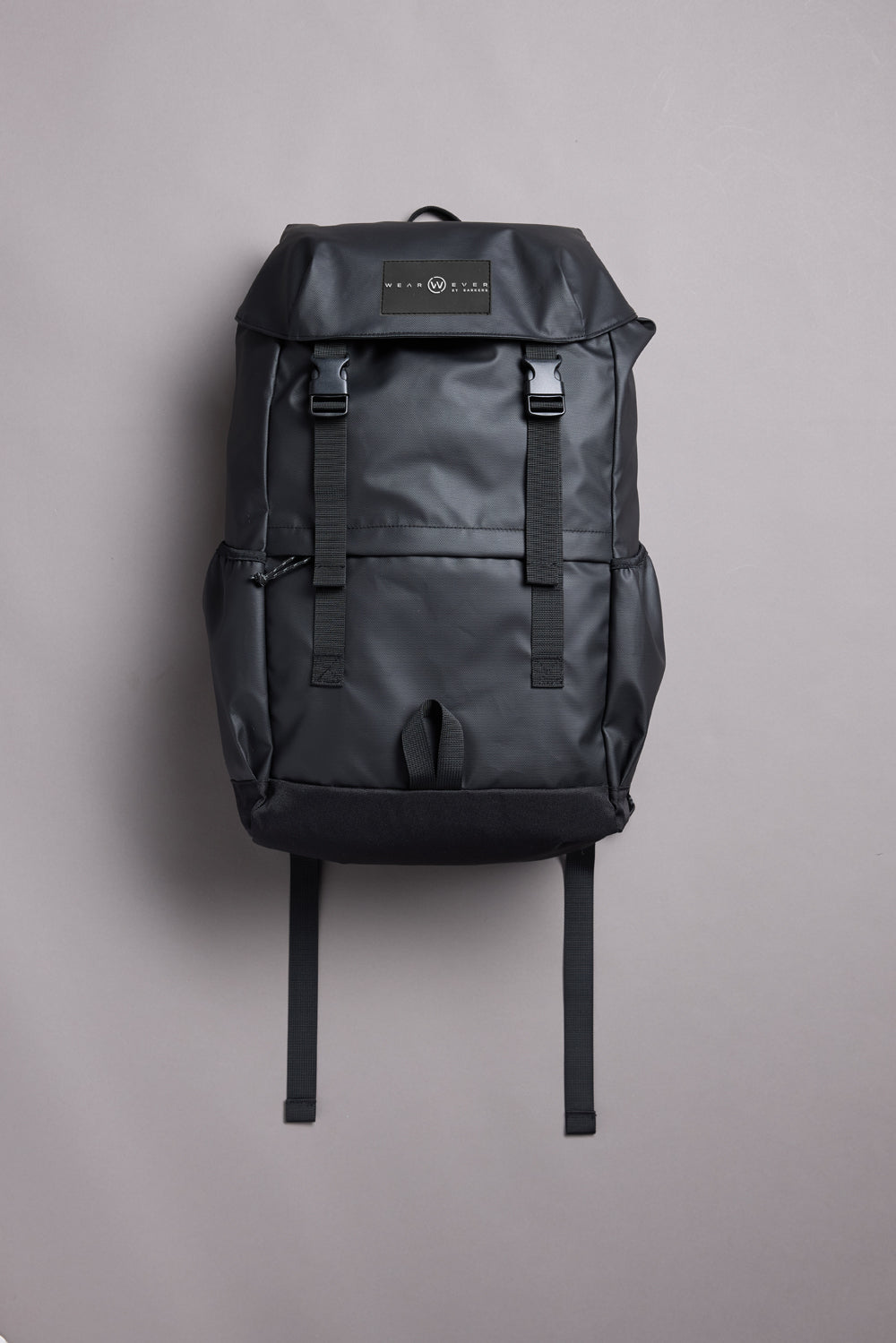 The WearEver Transit Backpack by WearEver is a sleek black bag with a top flap, two front buckles, side pockets, water-resistant zips, and a logo patch on the flap, shown upright on a plain light gray background.