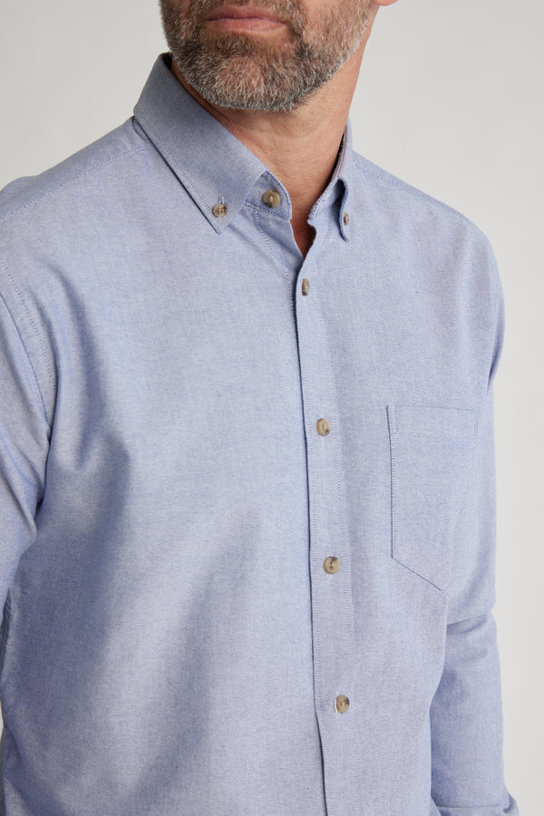 A man with a short beard wears the Barkers Thatcher Oxford Shirt in light blue, featuring a front pocket and brown buttons. The tailored fit accentuates his chest and shoulders; only his lower face is visible.