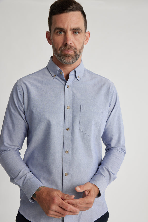 A man with short dark hair and a trimmed beard wears the Barkers Thatcher Oxford Shirt, featuring a tailored fit, chest pocket, and light blue responsibly sourced cotton. He stands against a plain background, looking at the camera with a neutral expression.