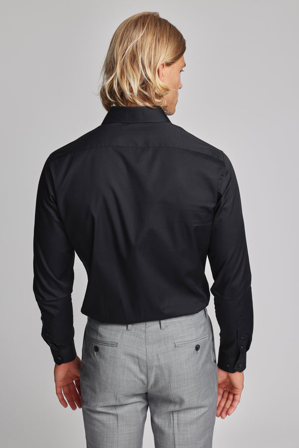 A person with shoulder-length blond hair wears a Barkers Tribeca Reg Cuff Shirt in black and light gray tailored dress pants, standing facing away from the camera against a plain light background.