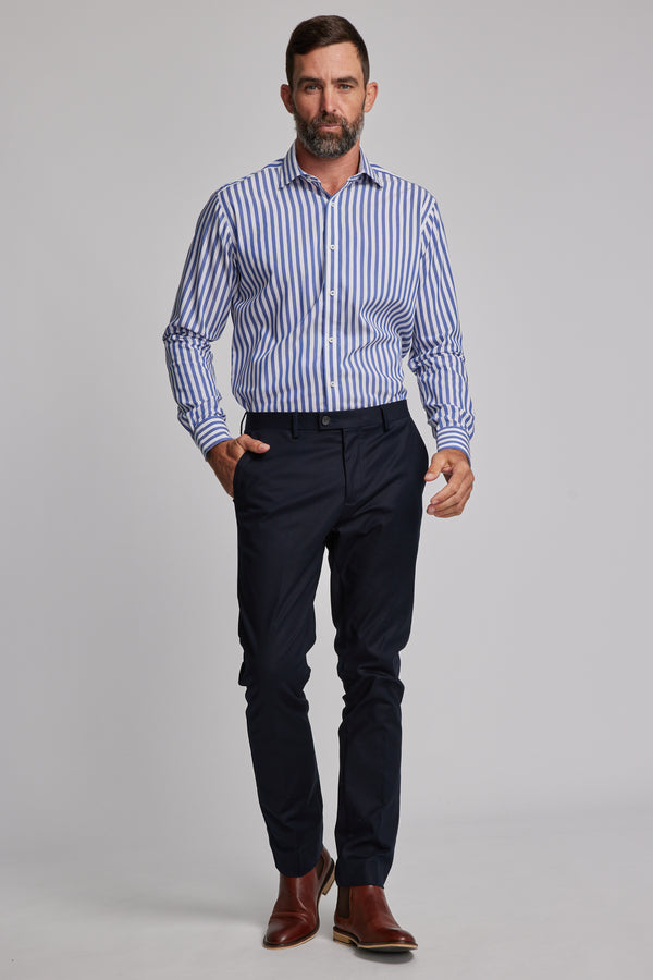 A man with short brown hair and a beard wears the Barkers Midway Shirt in a tailored fit, paired with dark navy dress pants and brown dress shoes, walking confidently against a plain light gray background.