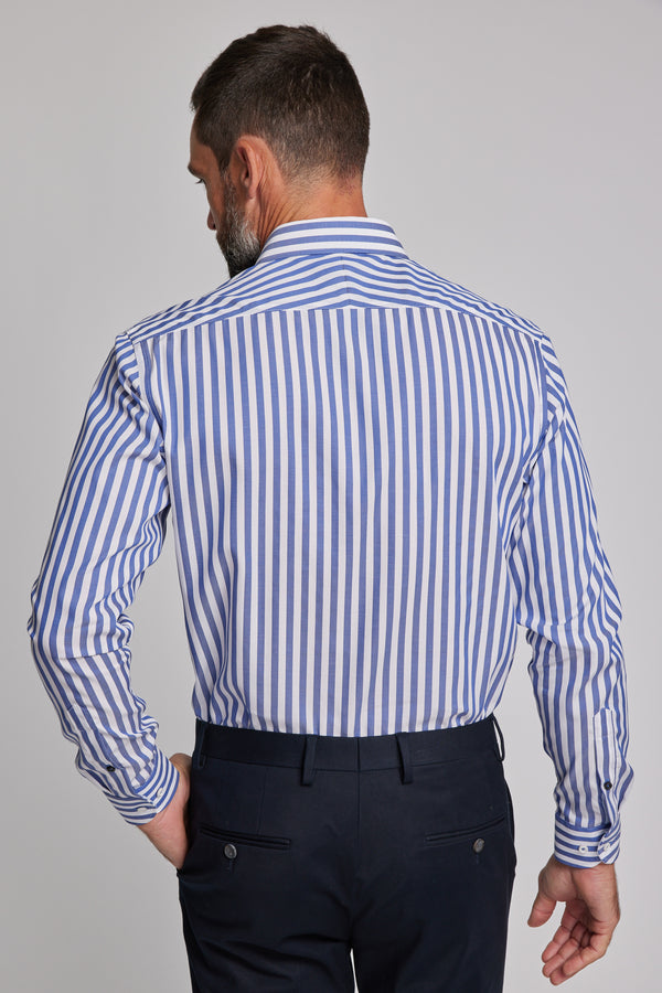 A man faces away from the camera, dressed in Barkers’ Midway Shirt—blue striped, tailored fit—and dark trousers, with his left hand in his pocket.