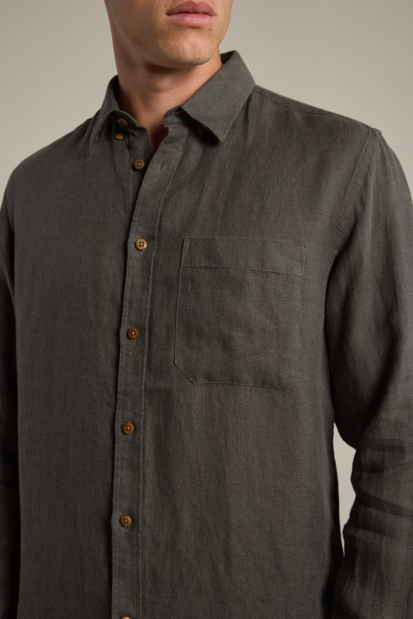 A man wears the Barkers Delano Linen Shirt in dark grey, featuring a classic fit with a collar and chest pocket, shown from shoulders to waist against a plain background.