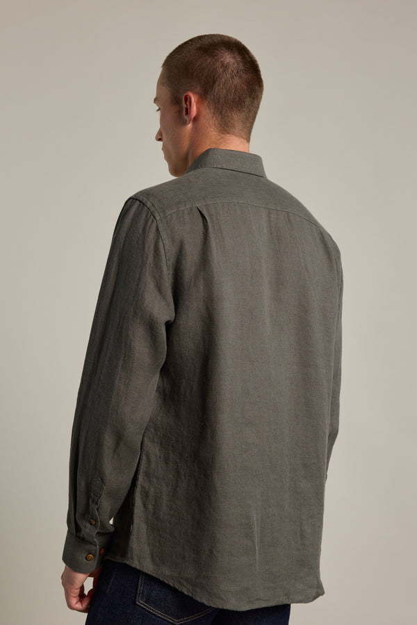 A person with short hair, wearing the Barkers Delano Linen Shirt in gray and dark jeans, stands facing away from the camera against a plain light background.