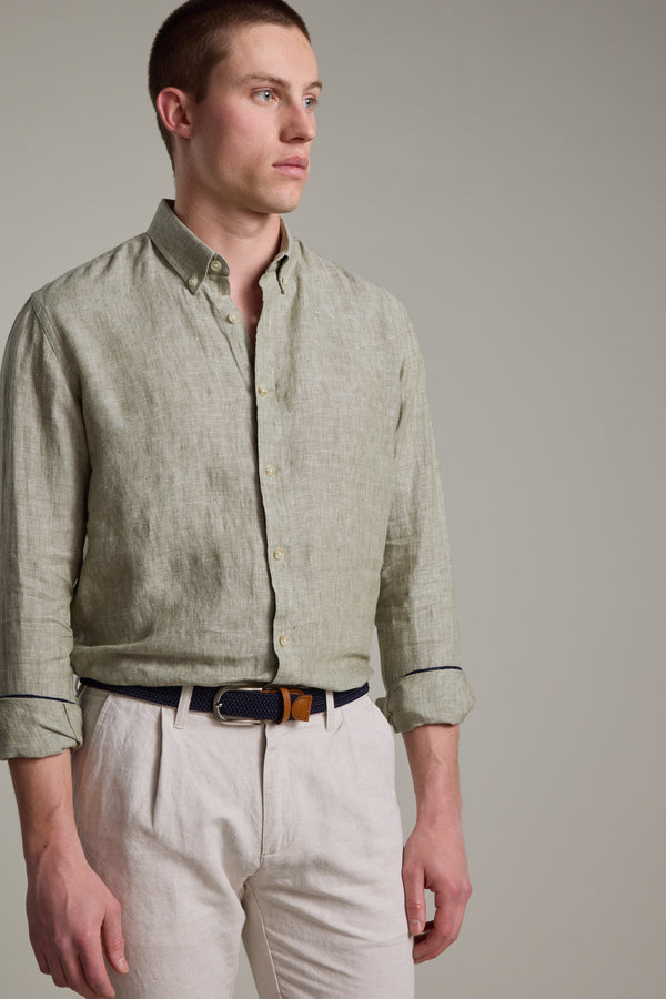 A man wears the Barkers Dorset Linen Shirt in light green—breathable French linen with a tailored fit, sleeves rolled up—paired with beige trousers, standing against a plain light gray background and looking to the side.