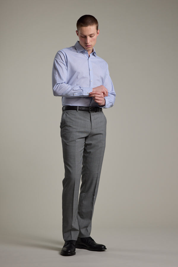 A man stands against a neutral background wearing the Barkers Seton Print Business Shirt, grey dress pants, a black belt, and black shoes, looking down as he adjusts his shirt cuff.