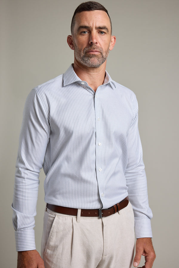 A man with short hair and a trimmed beard wears the Barkers Clarke Stripe Business Shirt in a tailored fit, tucked into beige pants with a brown belt, standing against a plain background.