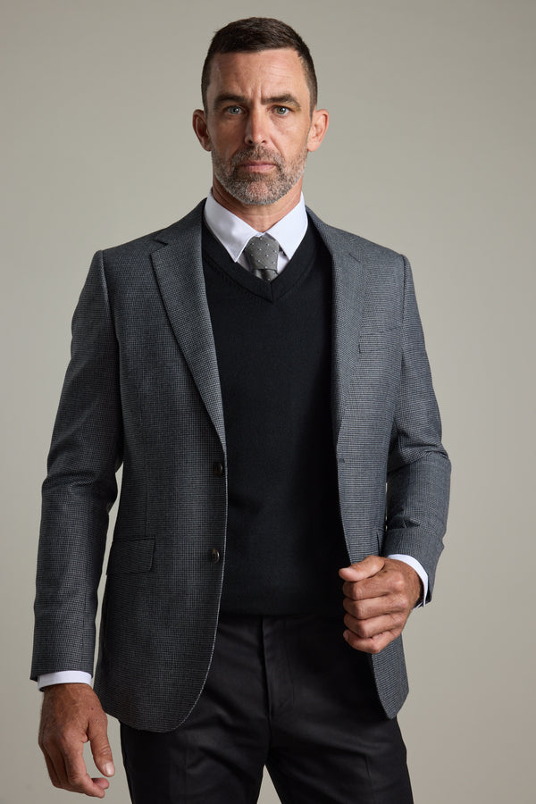 Man wears Barkers Skyland ZQrx Merino Vee sweater with suit and tie against plain background.