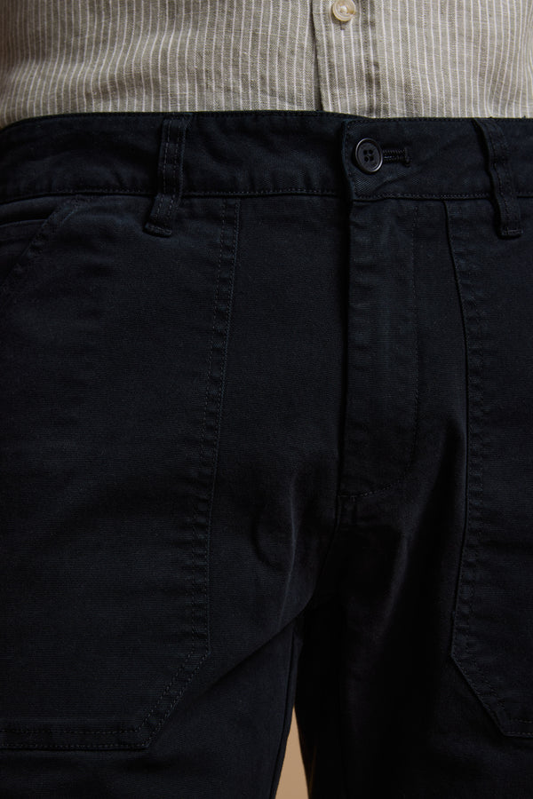 Close-up of a person wearing Barkers Tidal GD Utility Shorts in navy, featuring garment-dyed cotton, button and belt loops, paired with a beige and white striped shirt tucked in.