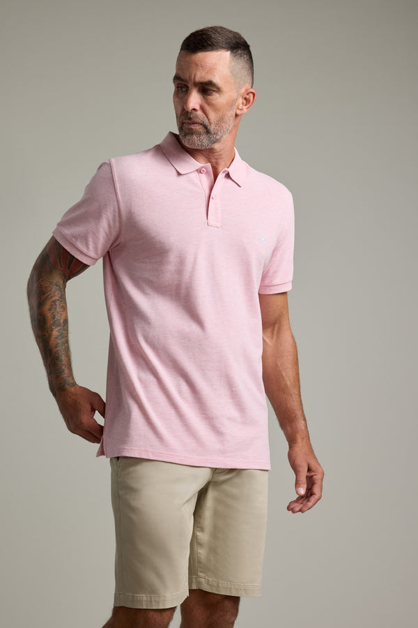 Man in a light pink Barkers Regent Pique Polo and beige shorts against a plain background.
