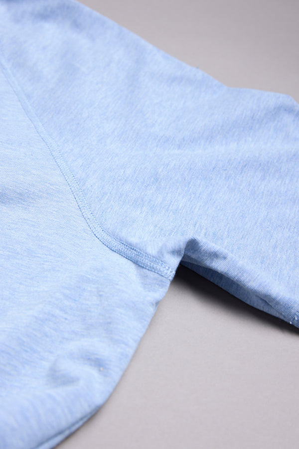 A close-up of the sleeve and side seam of a light blue WearEver Outbound Polo, a breathable cotton-blend shirt, laid flat on a neutral grey surface.